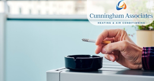 Close up of a hand holding a lit cigarette over an ashtray